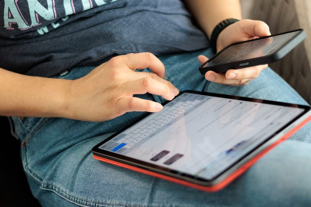 Close-up of adult using a tablet and smartphone indoors, showcasing digital connectivity and multitasking. Image from Pexels | IslandHopper X